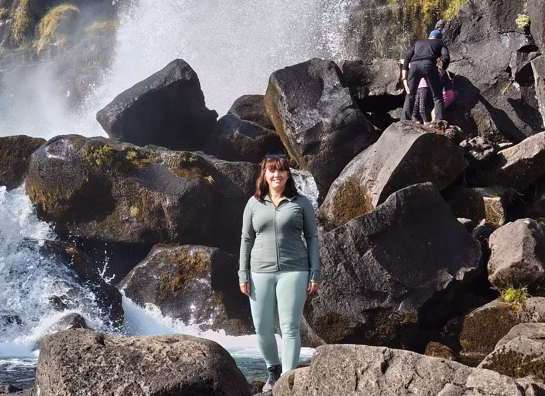 Woman in green athletic wear standing on volcanic rocks near a waterfall in Iceland