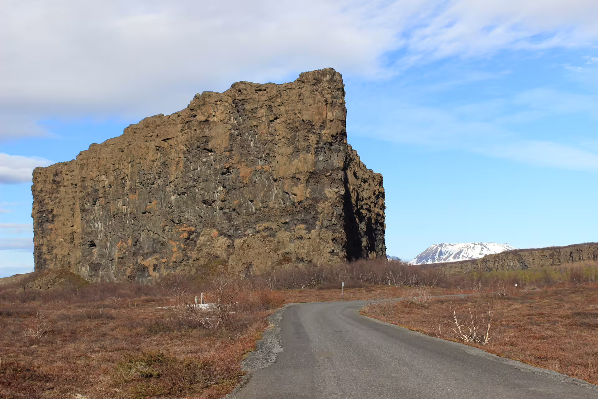 Massive basalt rock formation beside a narrow road in Iceland with snow-capped mountain in background