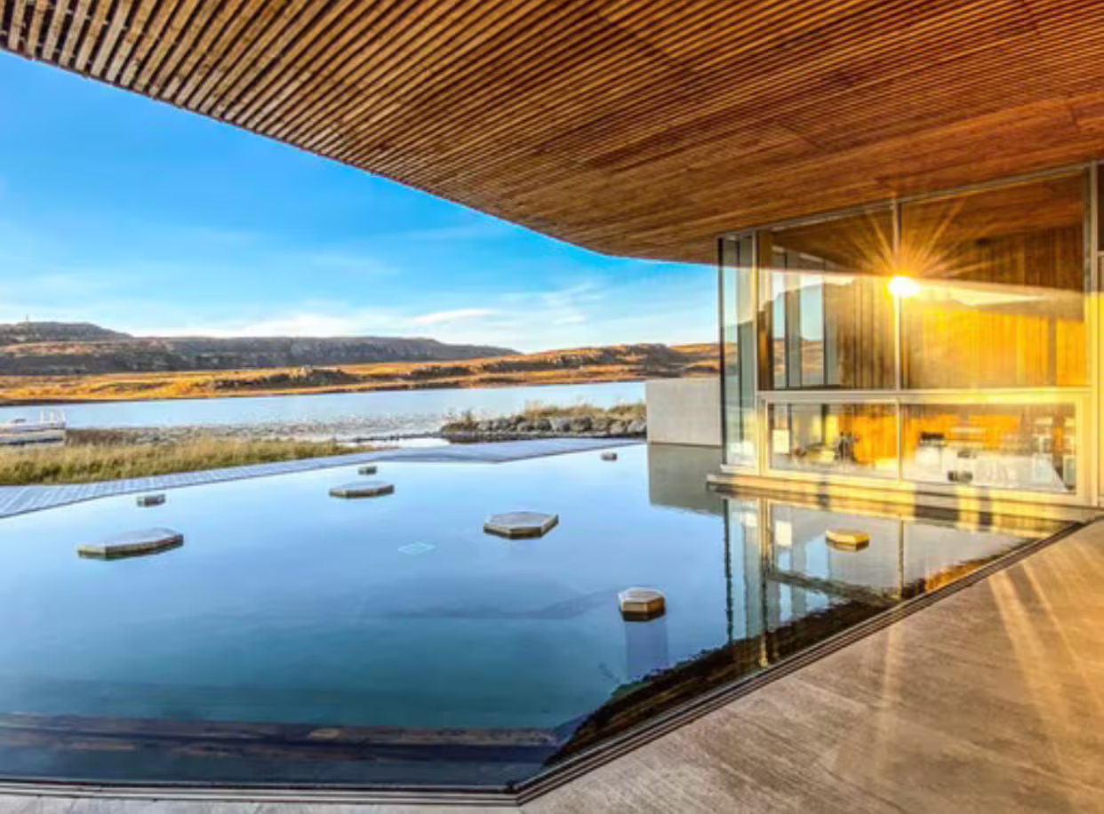 Luxury geothermal infinity pool with stepping stones overlooking Icelandic lake and volcanic landscape
