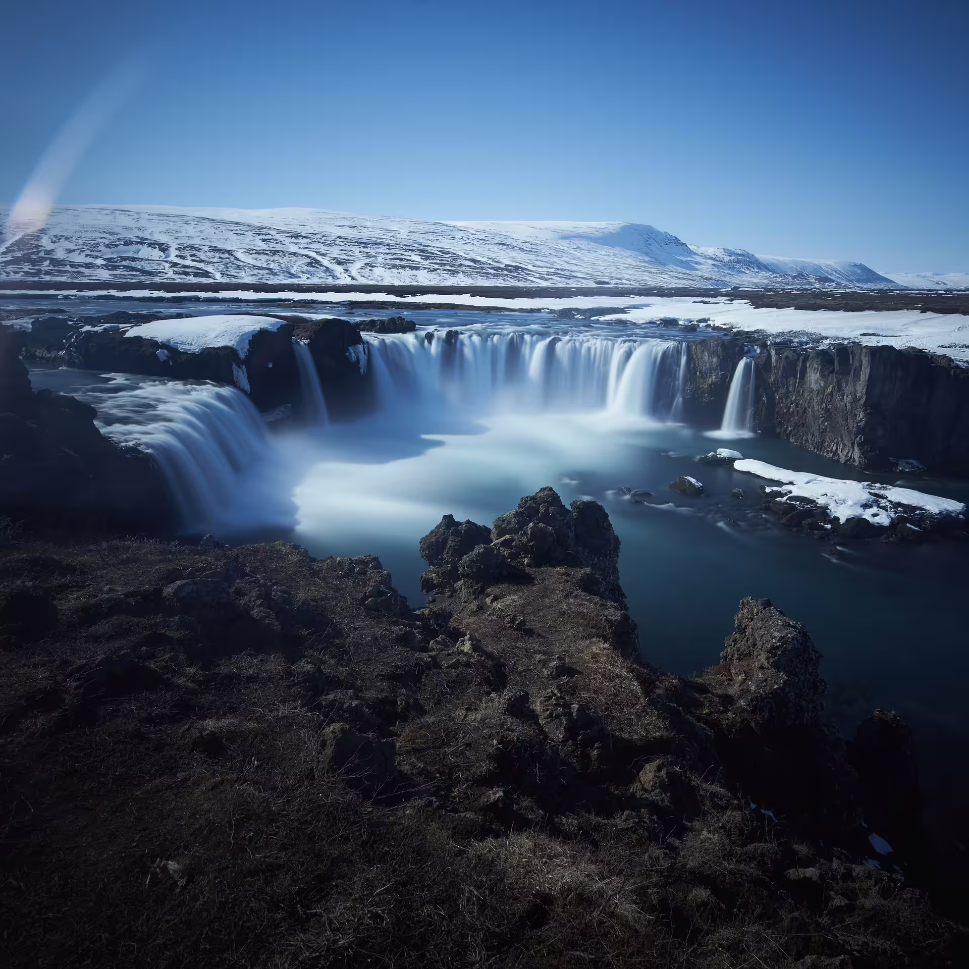 Godafoss waterfall cascading over snow-covered rocks in Iceland under a clear blue winter sky