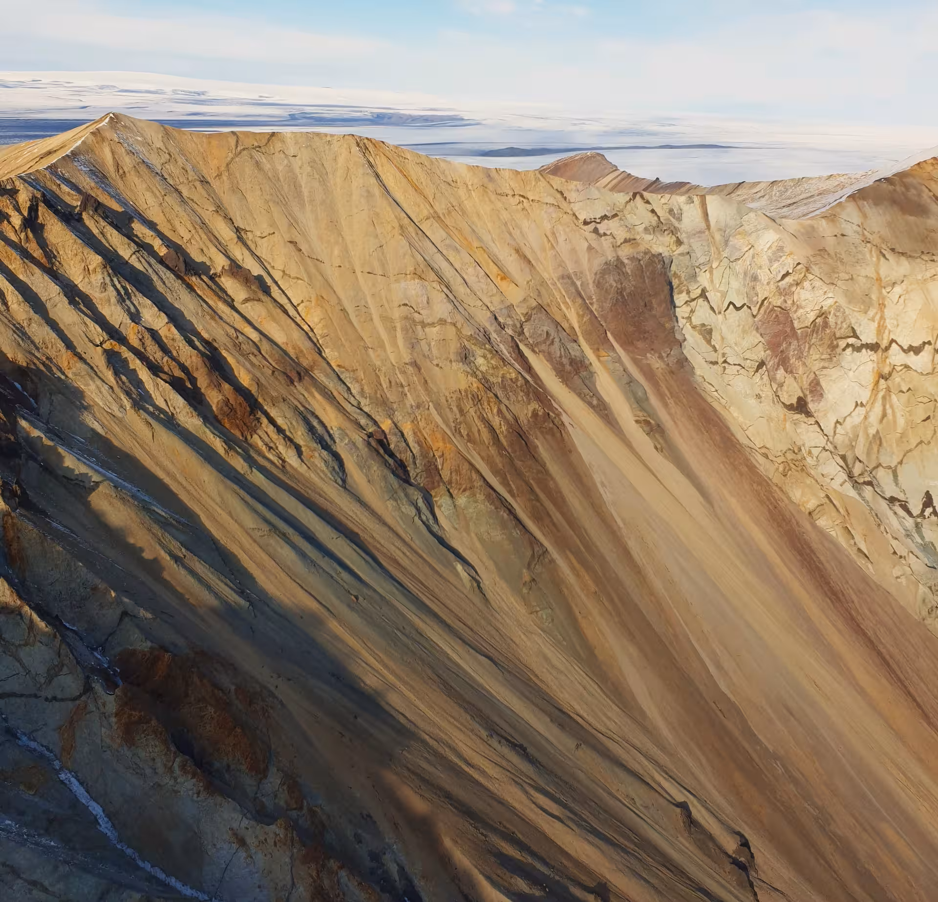 Aerial view of colorful striated mountain ridges with snow-covered glacier plateau in Iceland background