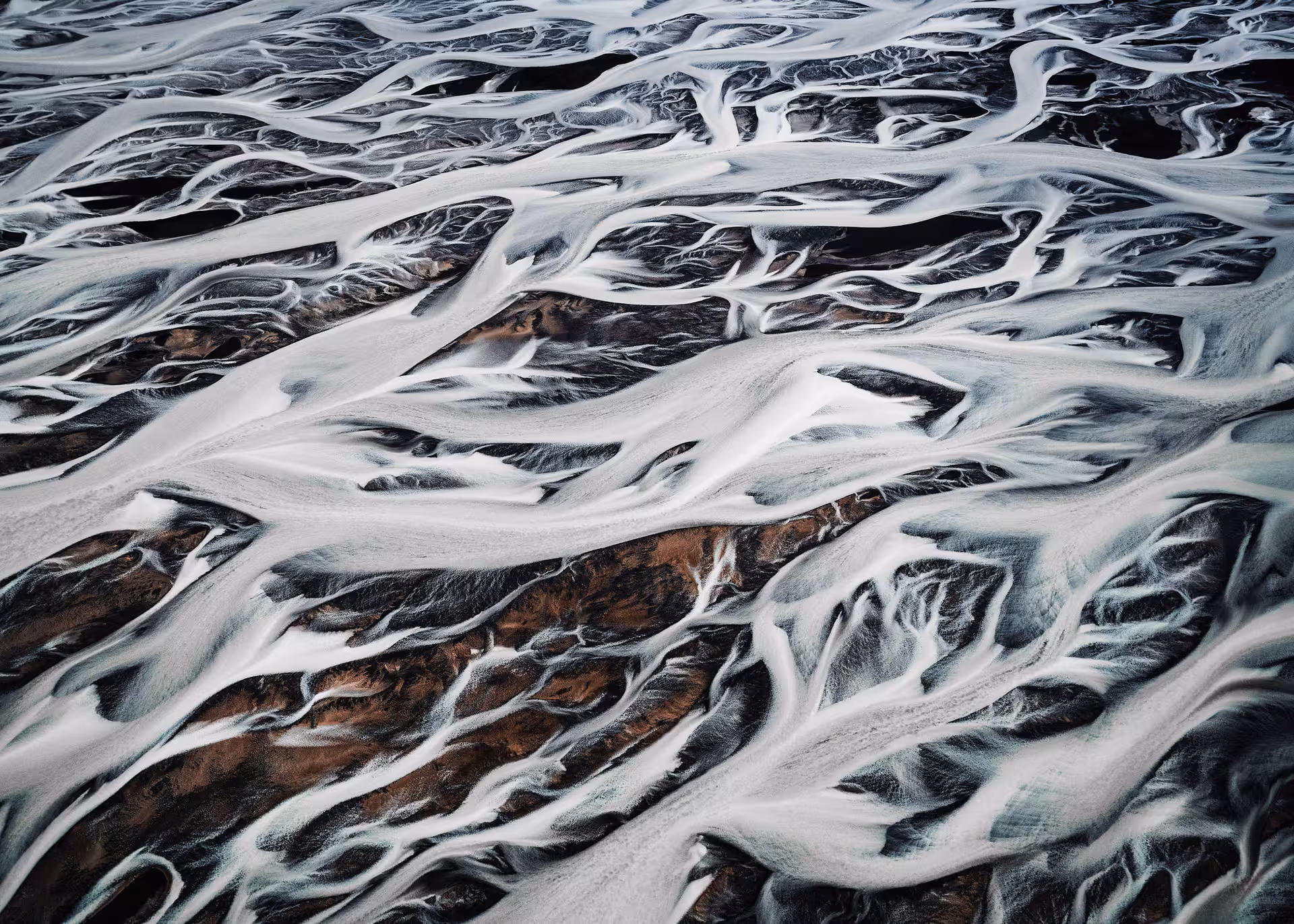 Aerial view of braided glacial rivers with white sediment flowing over colorful volcanic highlands in Iceland