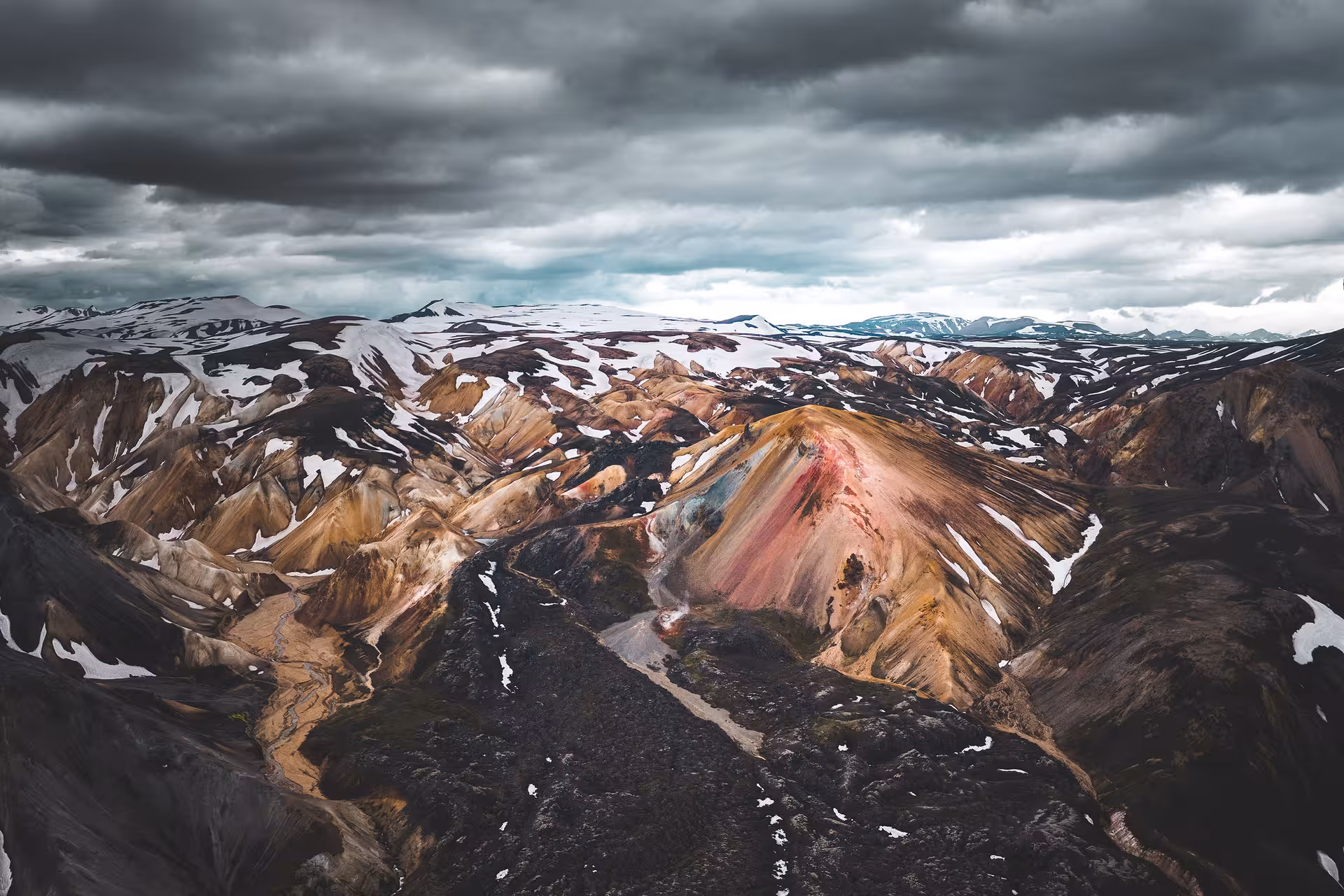 Aerial view of colorful rhyolite mountains with snow patches and dramatic clouds in Iceland's highlands
