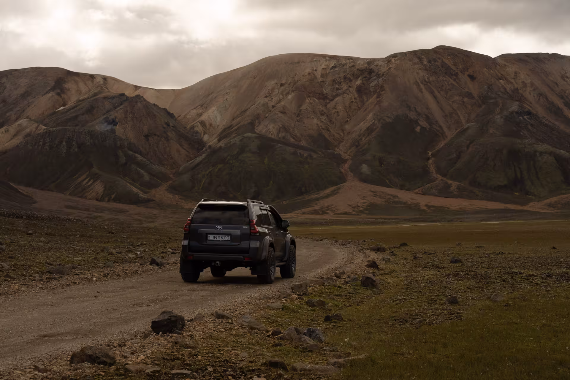 4x4 driving on an Iceland Highlands gravel road with Landmannalaugar rhyolite mountains under cloudy skies