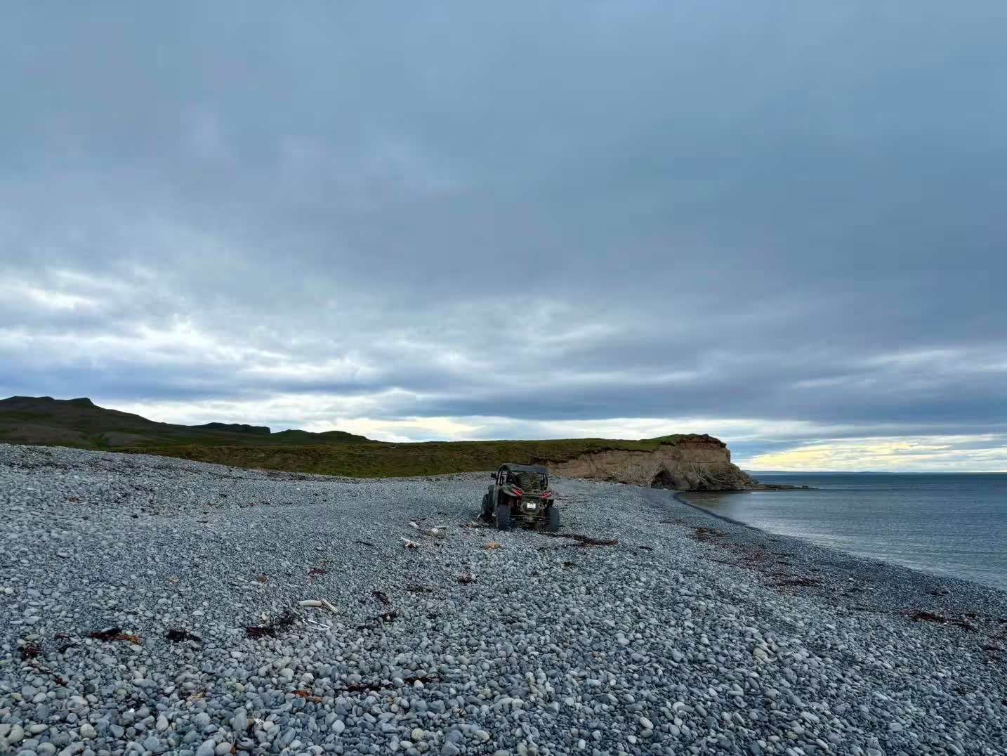 Buggy parked on rocky Iceland coastline with green cliffs and overcast sky