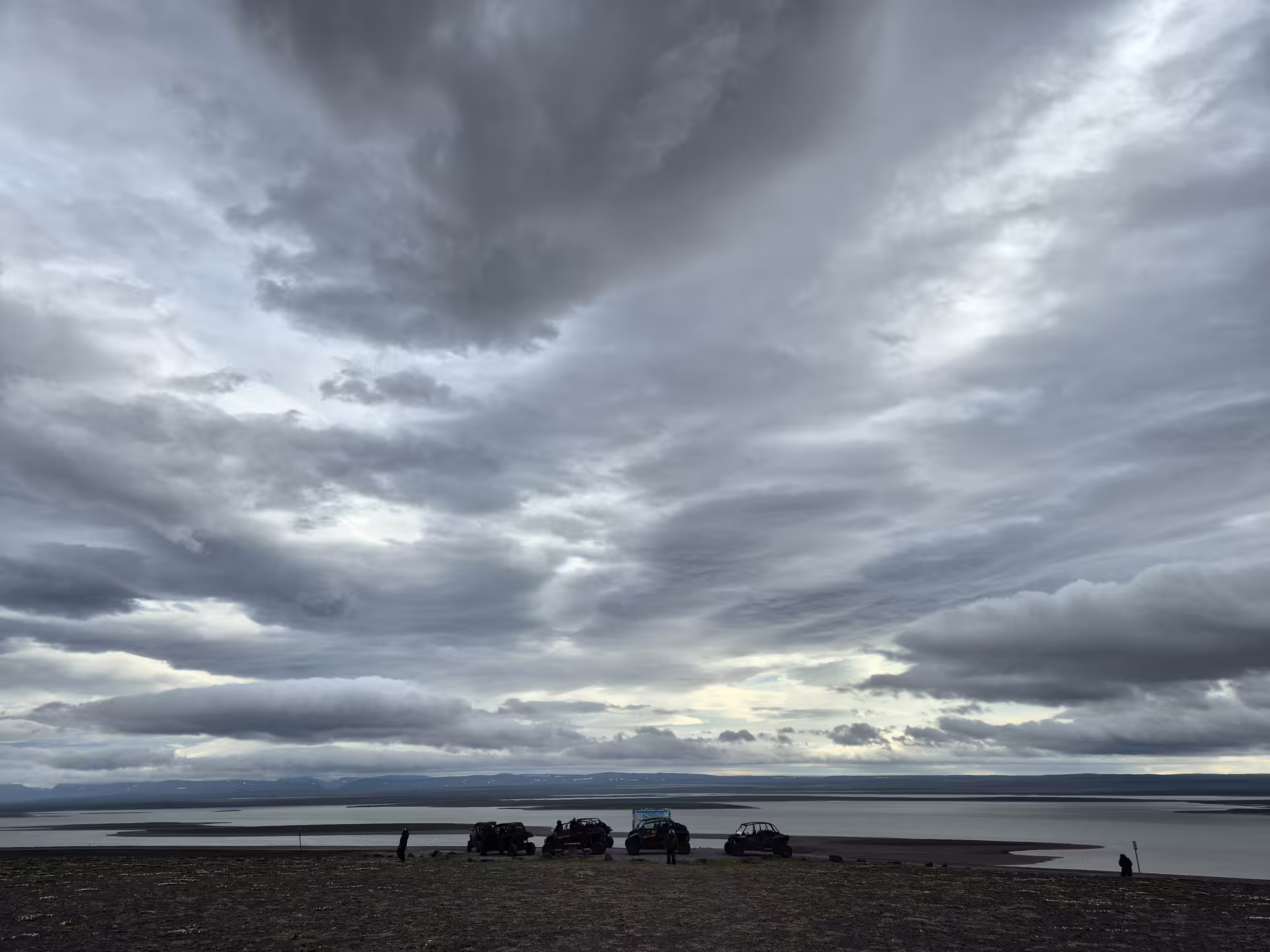 Off-road buggies and jeeps parked by a glacial lake under dramatic stormy skies in Iceland highlands