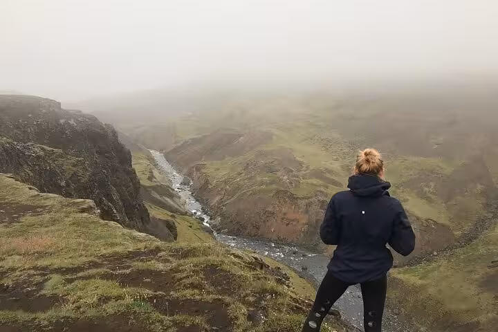 Hiker overlooking a deep canyon with a river winding through green Iceland highlands in misty fog