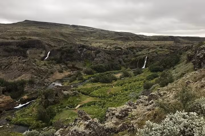 Lush green canyon with multiple waterfalls cascading down rocky cliffs in the Iceland Highlands