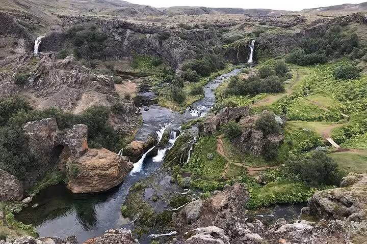 Iceland highlands canyon with cascading waterfalls, winding river, and lush green cliffs