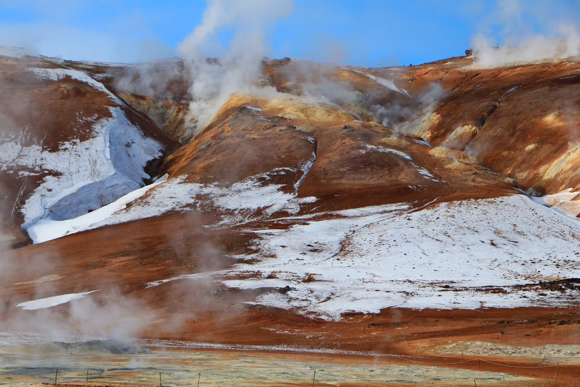 Steaming geothermal hills with snow and rust-colored volcanic terrain in Iceland's highlands