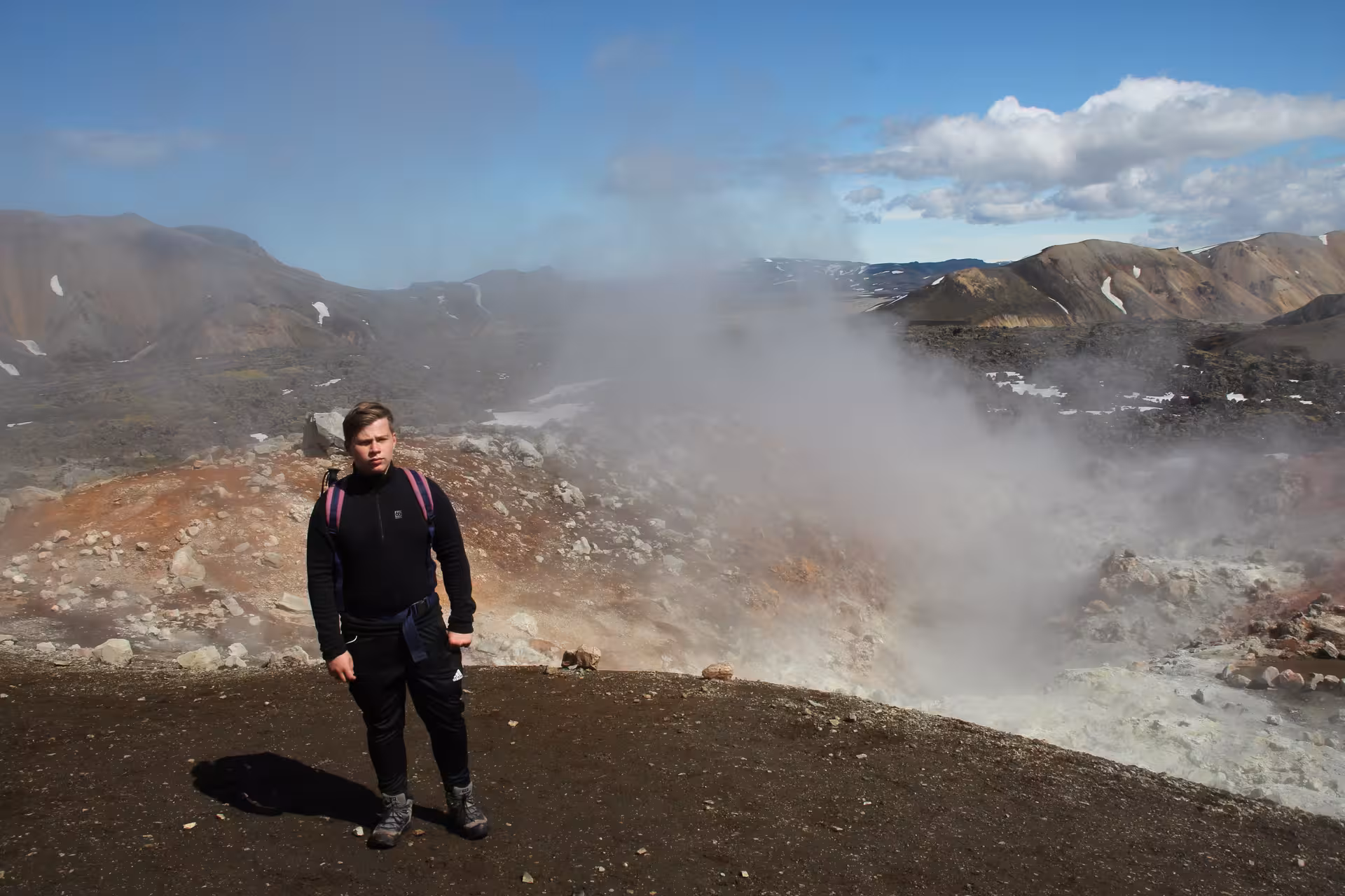 Hiker standing near steaming geothermal vents in Iceland Highlands volcanic landscape