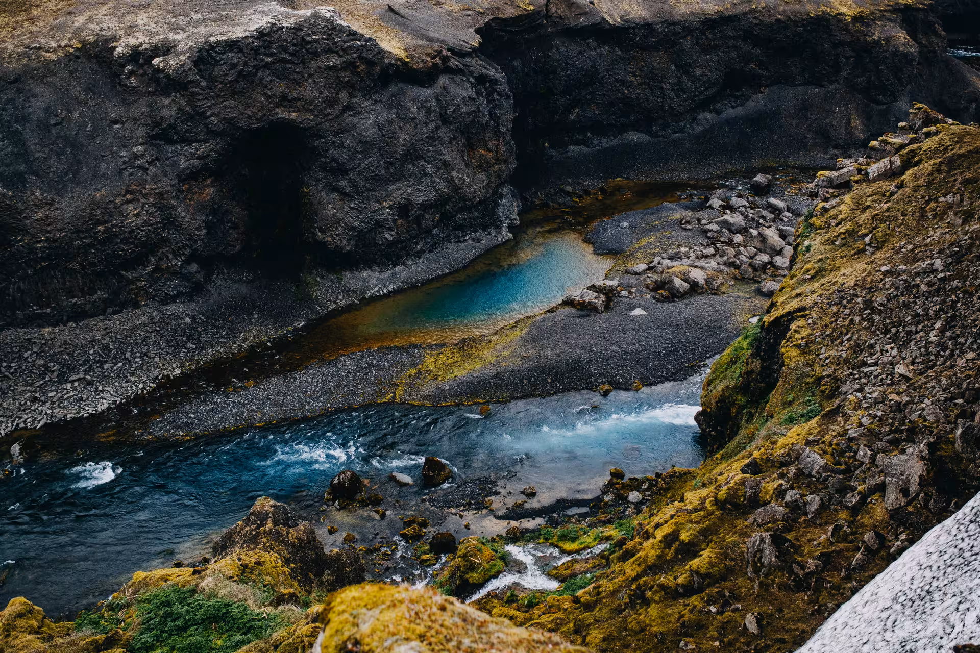 Turquoise glacial river pools winding through dark volcanic rock canyon in Iceland Highlands