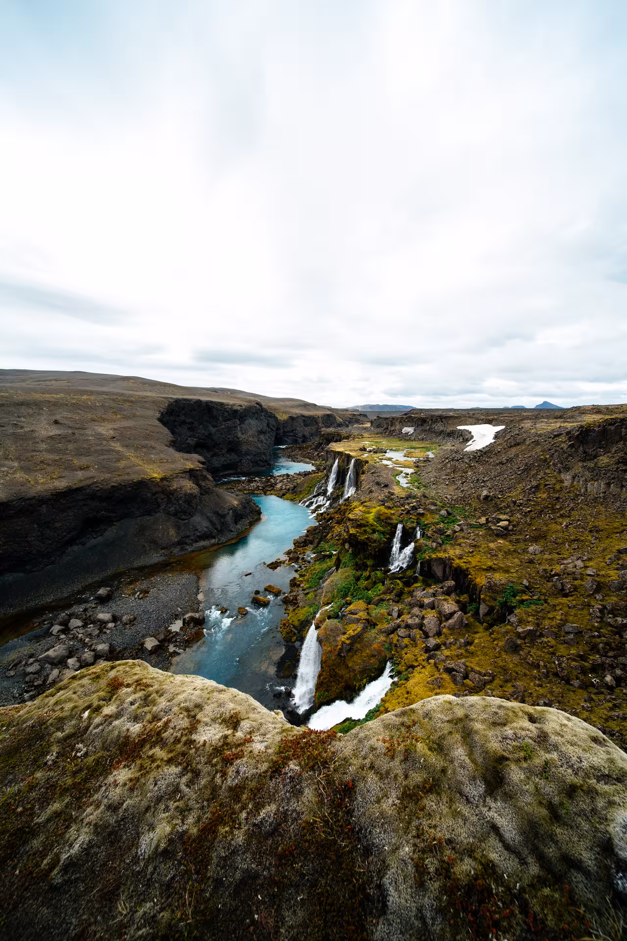 Turquoise glacial river with cascading waterfalls flowing through Iceland Highlands canyon