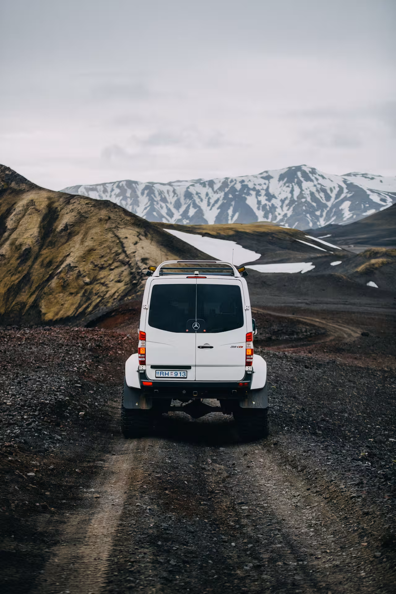 White Mercedes super jeep on gravel highland road with snow-capped mountains in Iceland