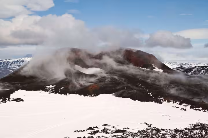 Snow-covered volcanic crater with mist and red lava rock in Iceland Highlands under blue sky