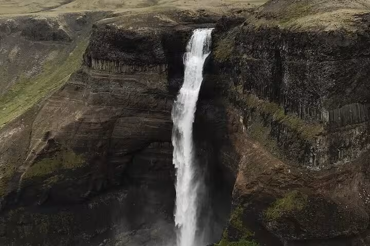 Tall waterfall cascading over dark basalt cliffs in Iceland's highlands canyon