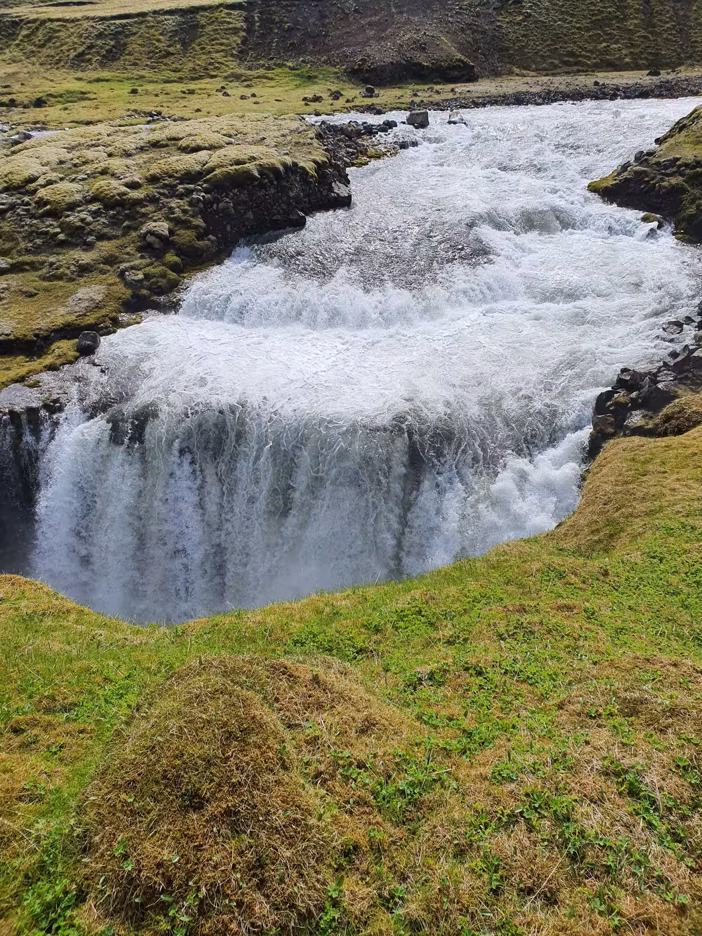 Powerful waterfall cascading over rocky ledge surrounded by green mossy landscape in Iceland Highlands