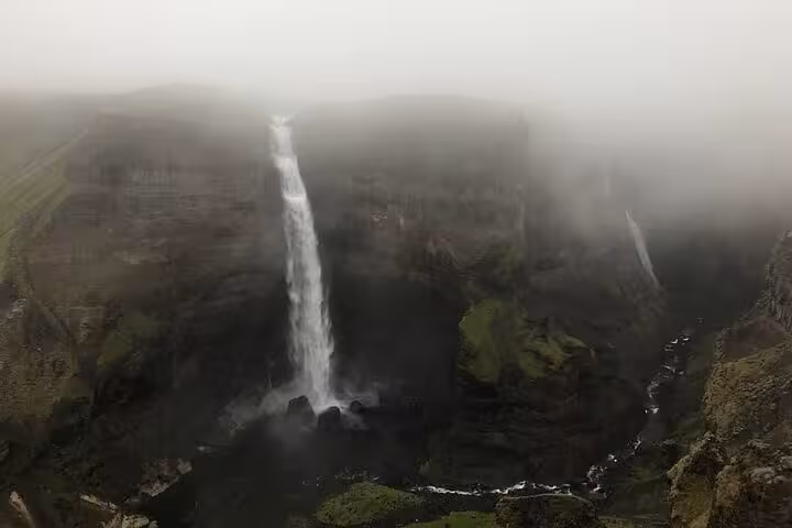 Tall waterfall cascading into misty canyon surrounded by green cliffs in Iceland Highlands