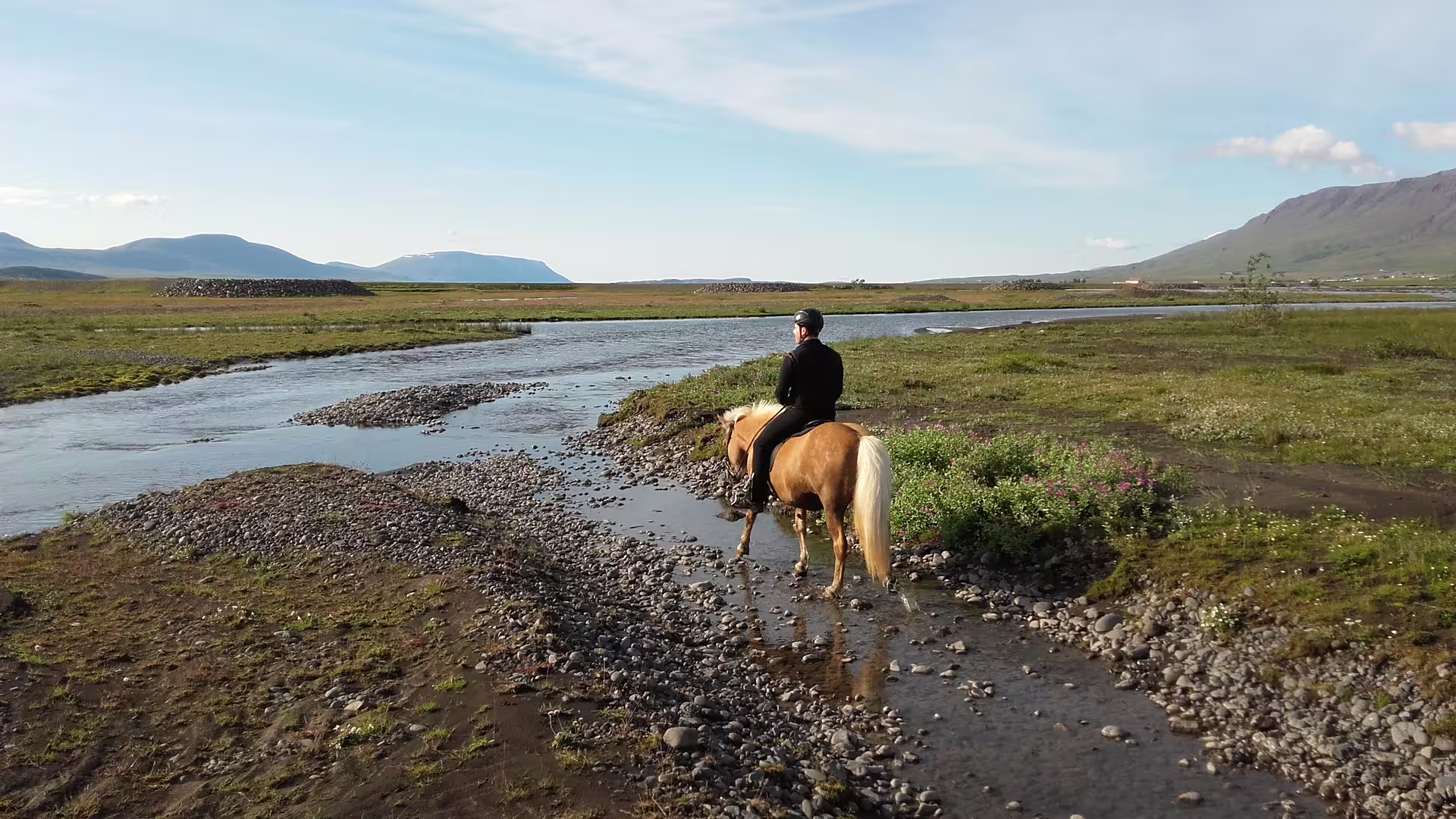 Rider on Icelandic horse crossing shallow glacier river delta with mountains in background
