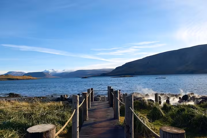 Wooden boardwalk leading to a serene fjord with mountains and geothermal steam in Iceland