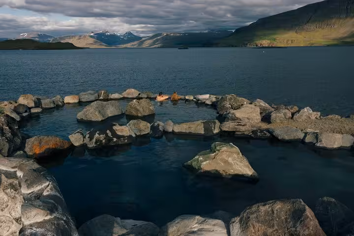 Natural hot spring pool surrounded by rocks overlooking a fjord with snow-capped mountains in Iceland