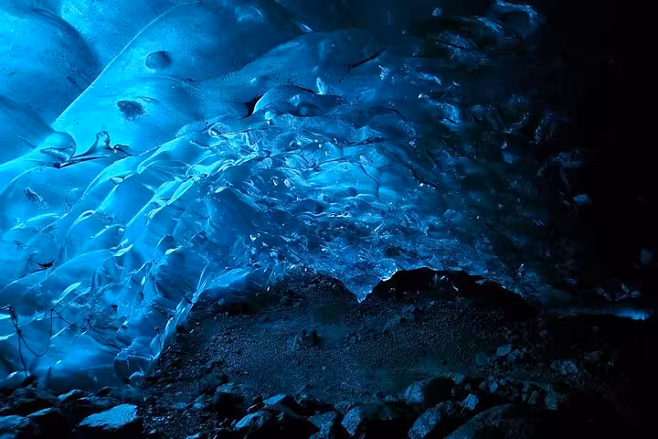 Glowing blue ice cave ceiling with rocky floor inside an Icelandic glacier