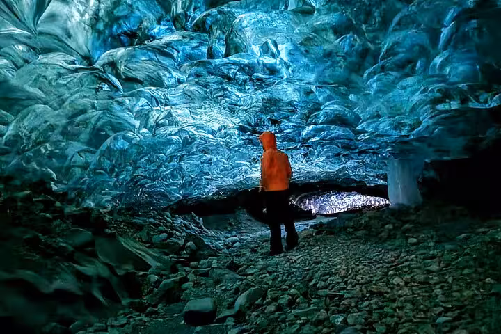 Explorer in red jacket standing inside a glowing blue glacial ice cave in Iceland