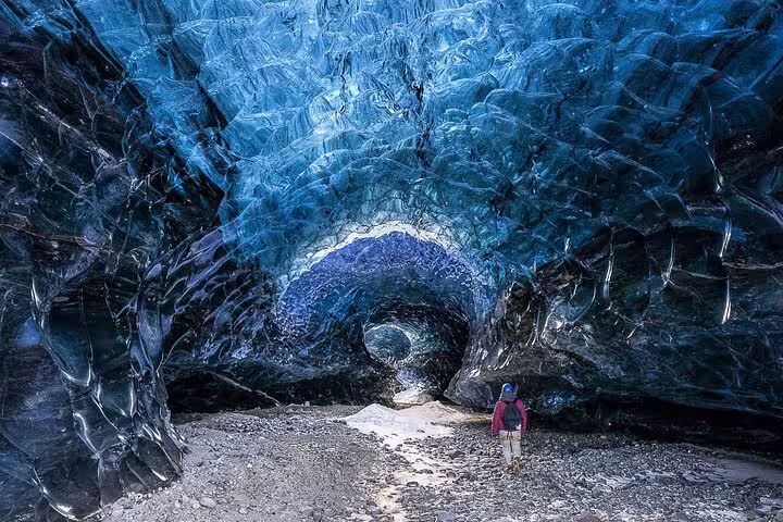 Hiker standing inside a stunning blue glacial ice cave tunnel in Iceland