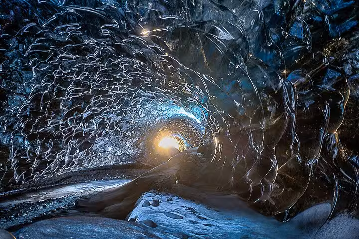 Glowing tunnel inside an Icelandic glacier ice cave with blue crystalline walls and volcanic rock floor