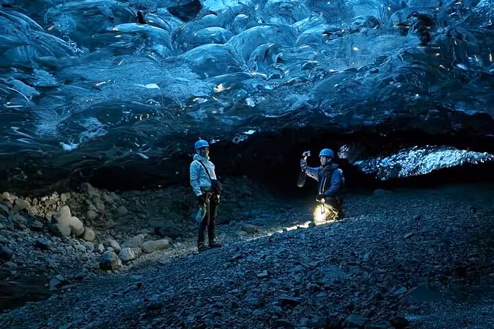 Two explorers in helmets photographing blue glacial ice cave ceiling in Iceland