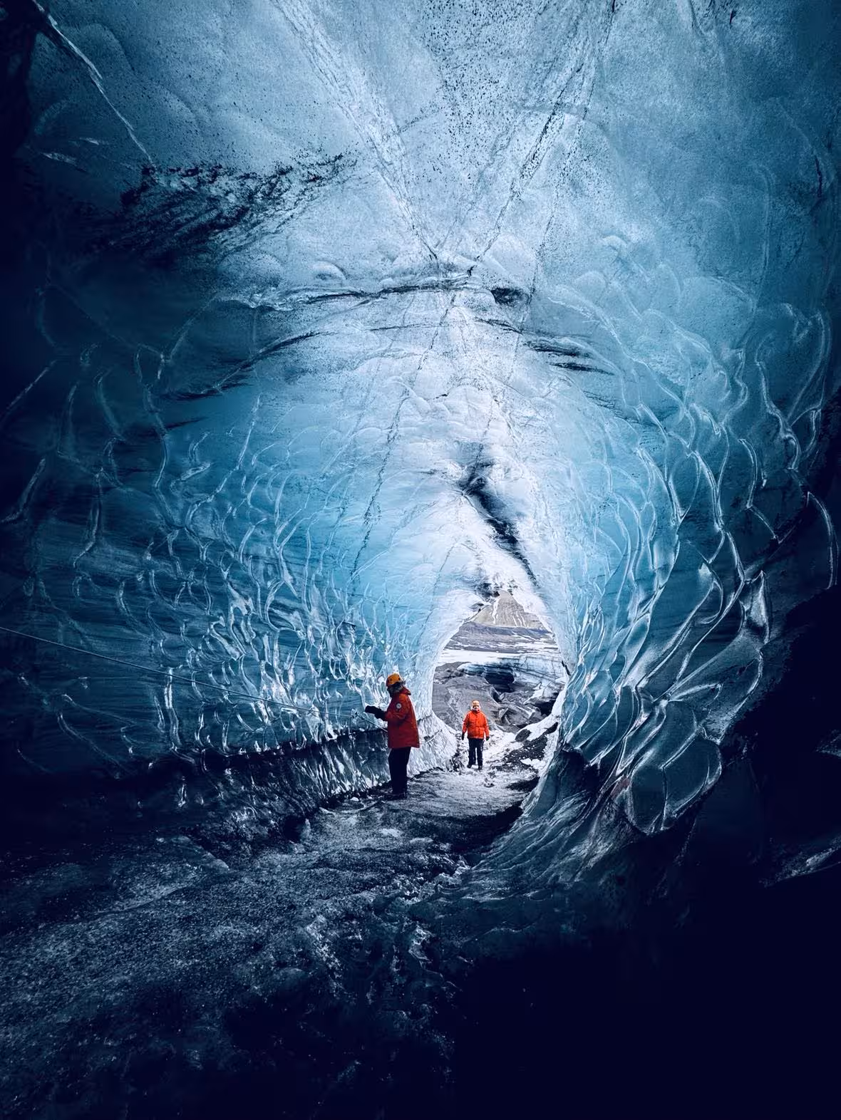 Two explorers in red jackets inside a stunning blue glacial ice cave in Iceland