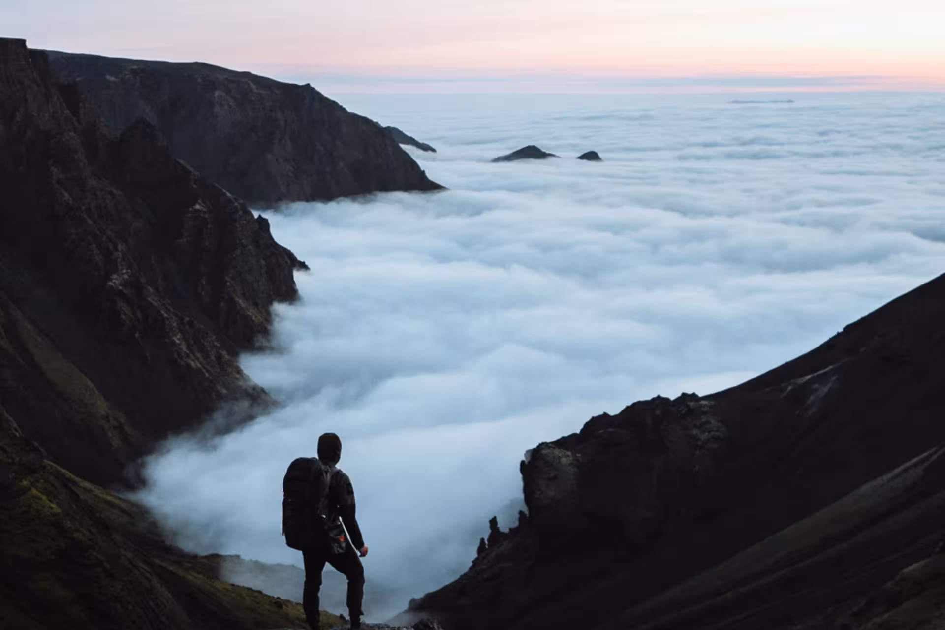 Hiker with backpack standing above sea of clouds on Iceland mountain trail at dusk