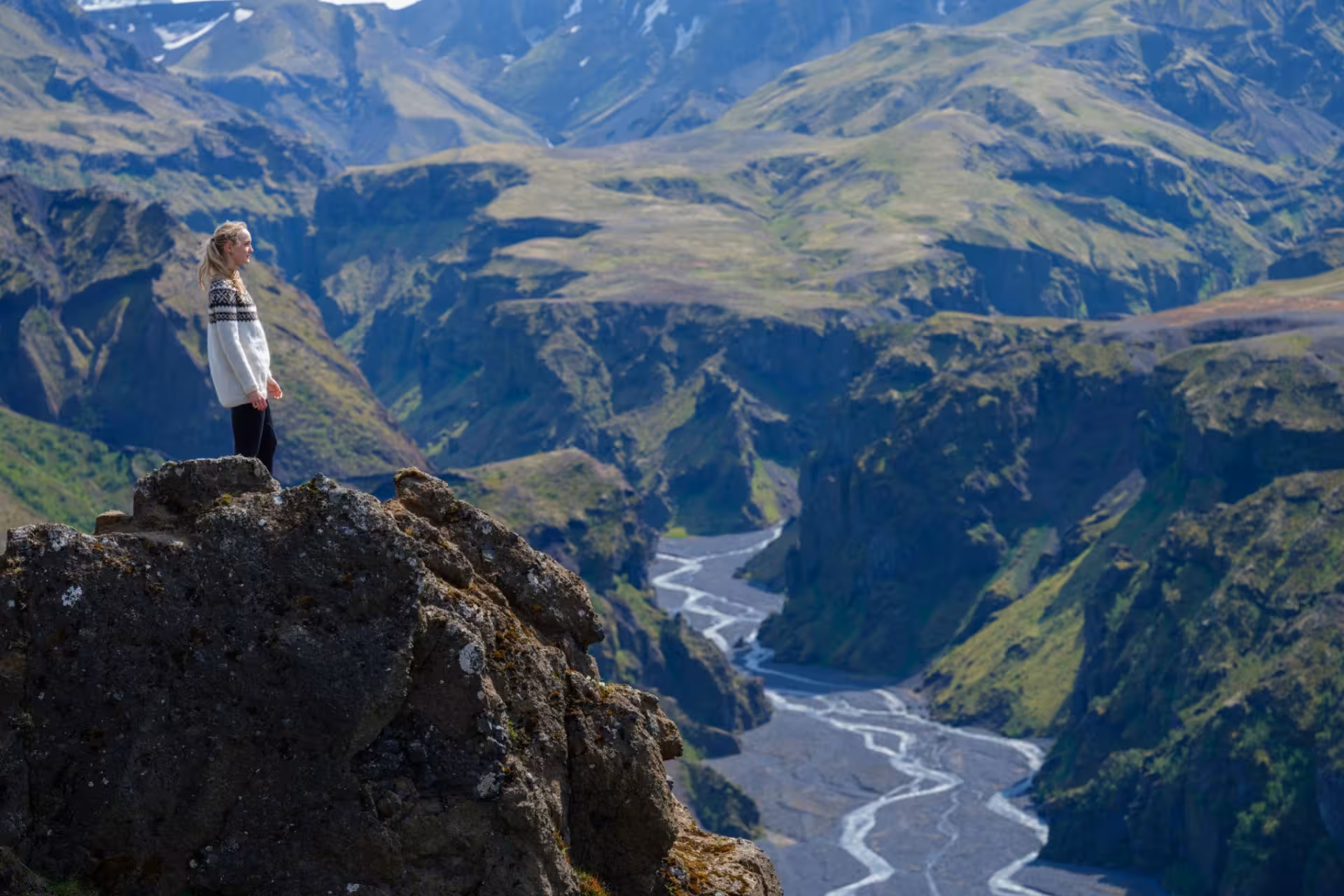 Hiker standing on rocky cliff overlooking Thorsmork valley and braided glacial river in Iceland