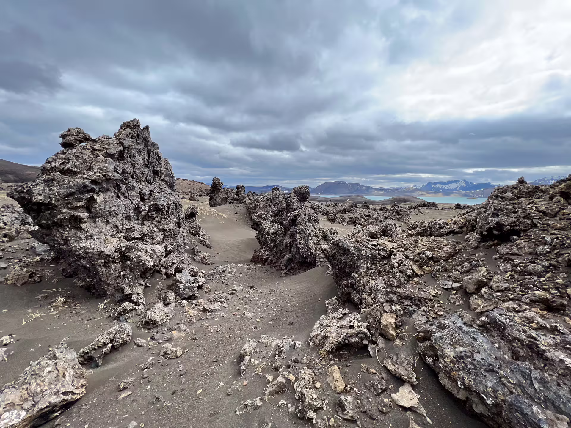 Rugged black lava rock formations with turquoise glacial lake and snow-capped mountains in background, Iceland