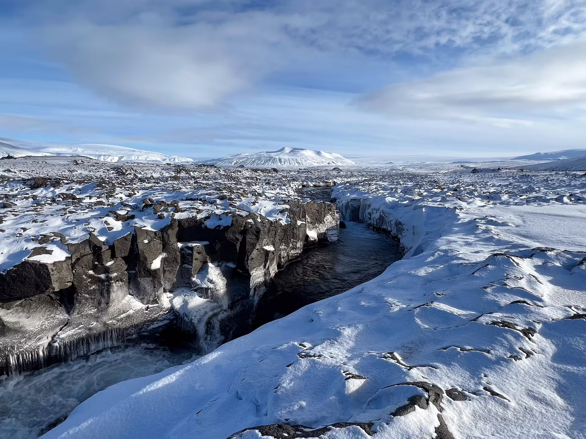 Snow-covered lava field with icy river canyon and volcanic mountains in Iceland winter landscape