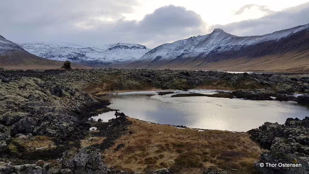 Snow-capped volcanic mountains and lava field with reflective pond in Iceland's highland landscape