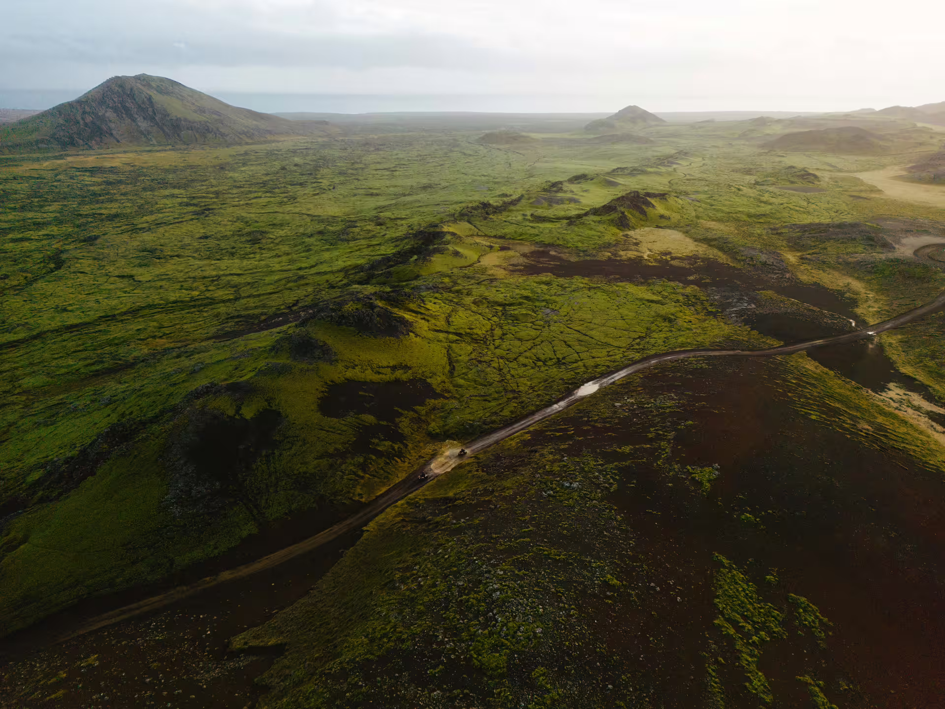 Aerial view of moss-covered lava fields with winding dirt road and ATV riders in Iceland