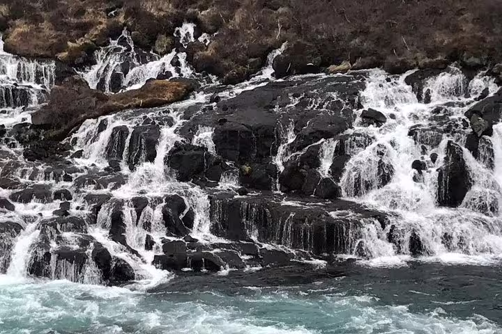 Cascading waterfalls flowing over black lava rock formations into turquoise river in Iceland