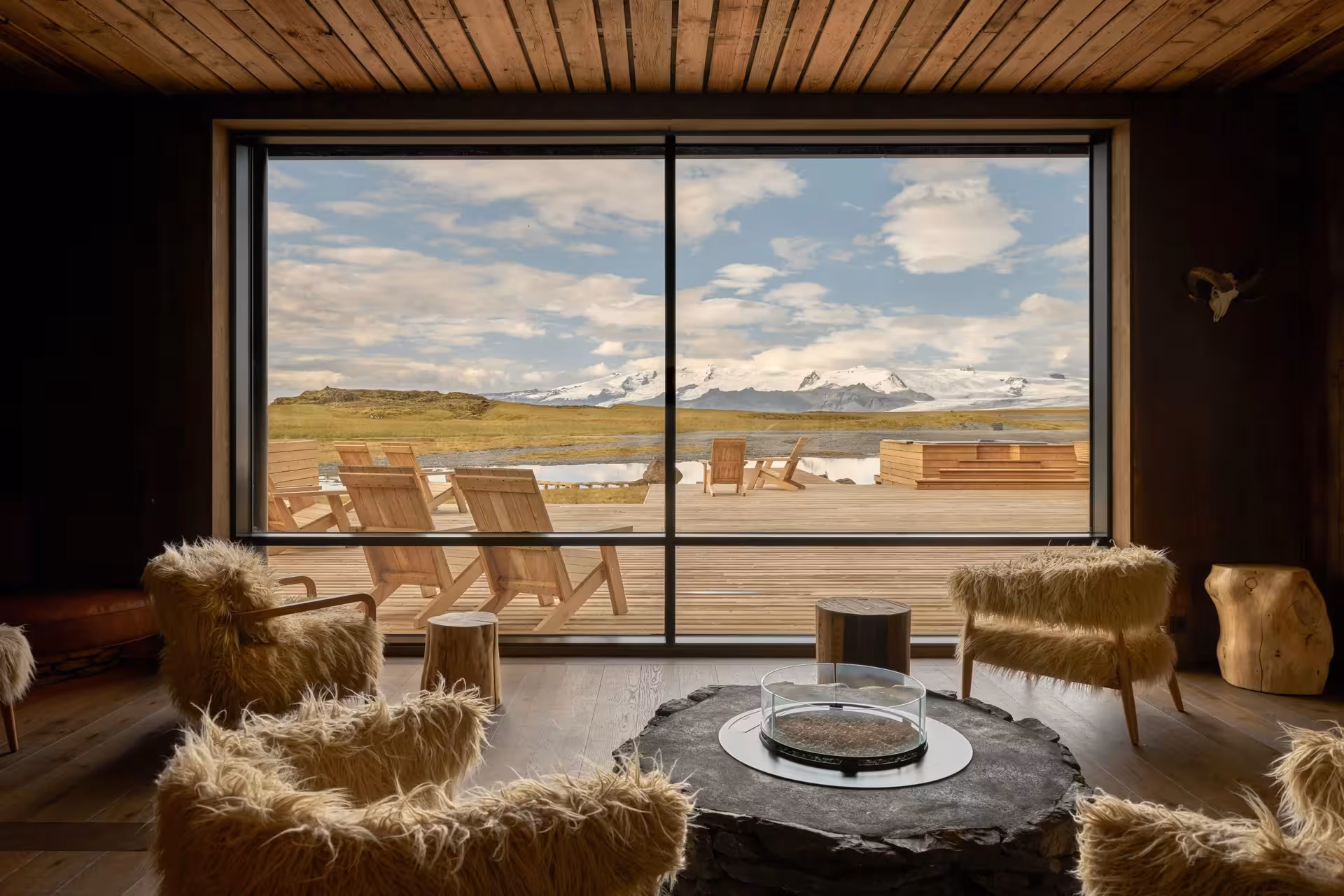 Cozy Iceland lodge interior with sheepskin chairs and panoramic glacier and snow-capped mountain views on sunrise proposal tour