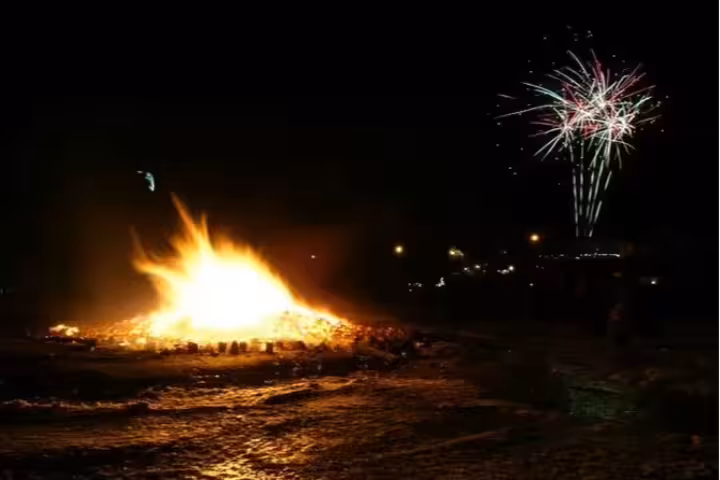 Large bonfire and colorful fireworks lighting the night sky in Iceland on New Year's Eve