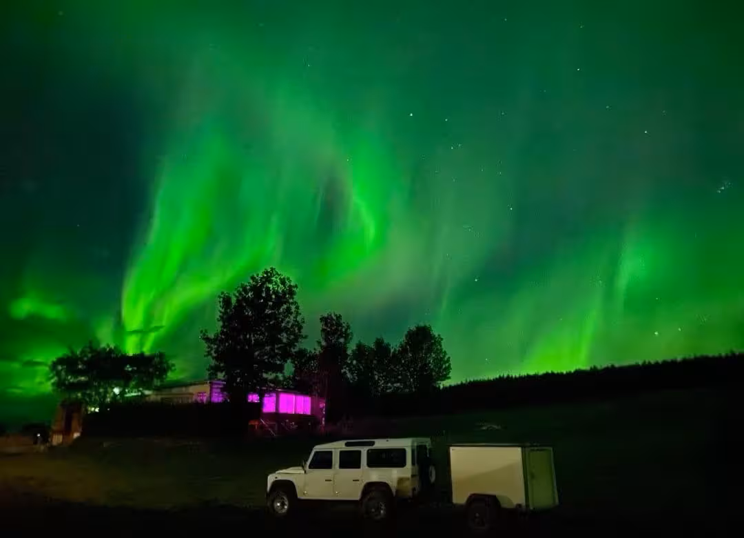 Vibrant green aurora borealis over a white Land Rover Defender with trailer in Iceland at night