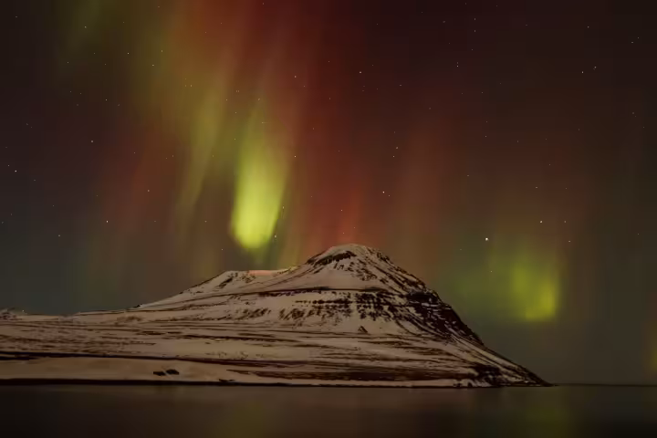 Vivid green and red aurora borealis dancing over a snow-capped mountain peak in Iceland at night