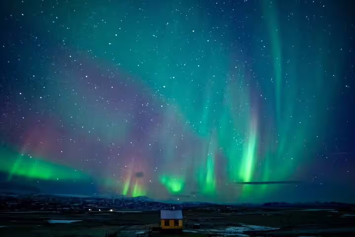 Vibrant green and purple aurora borealis dancing over a small house in Iceland at night