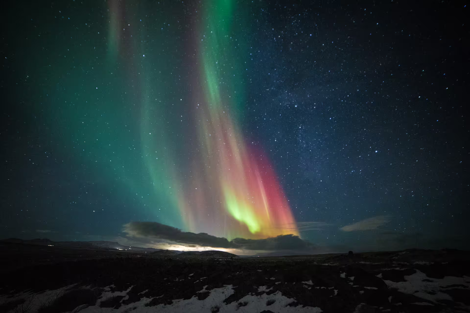 Vibrant green and red aurora borealis dancing over snowy Iceland landscape at night