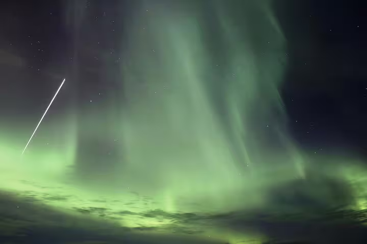 Vivid green northern lights aurora borealis with vertical pillars and meteor streak over Iceland night sky