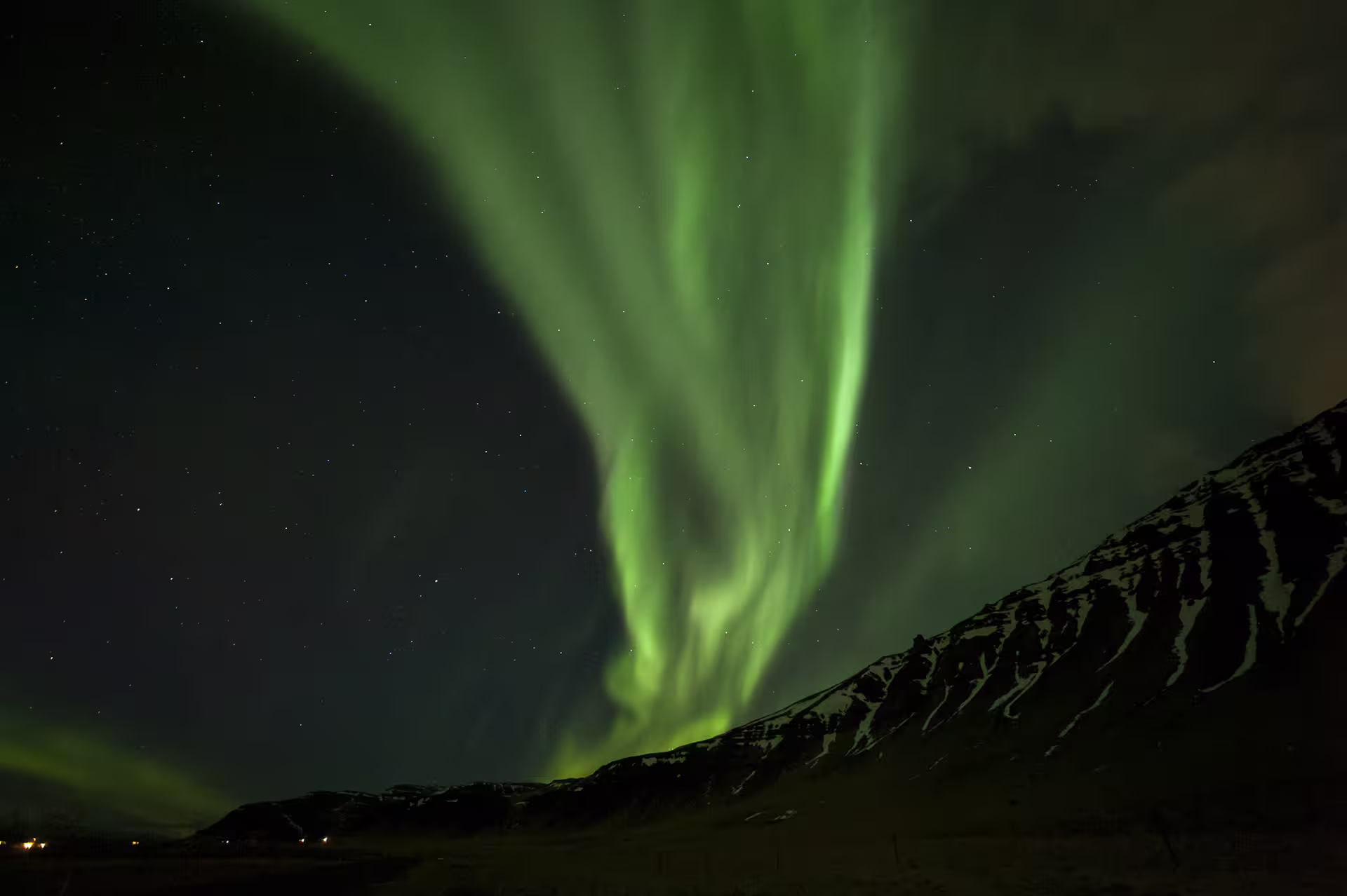 Vibrant green northern lights aurora borealis dancing over snow-capped mountains in Iceland at night