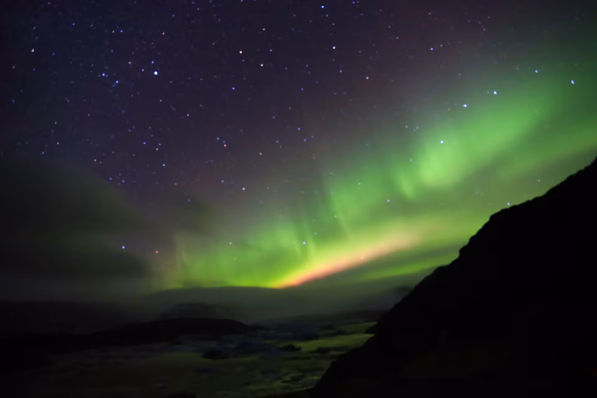 Vibrant green northern lights aurora borealis over Iceland's dark landscape and starry night sky