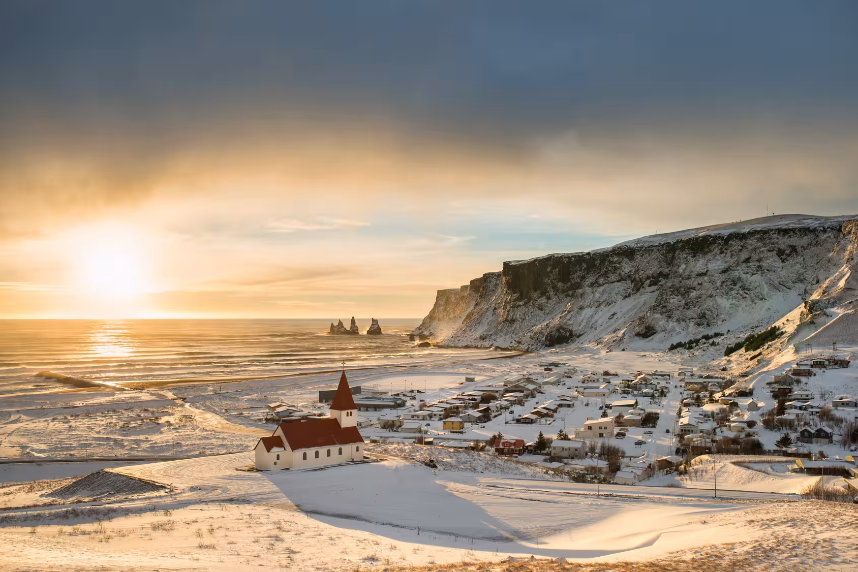 Scenic winter sunrise over Vik village, Iceland with snowy landscapes and ocean views.