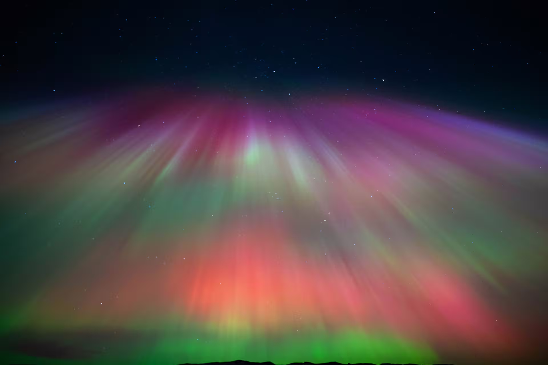 Vibrant aurora borealis with red, green, and pink rays radiating across Iceland's night sky