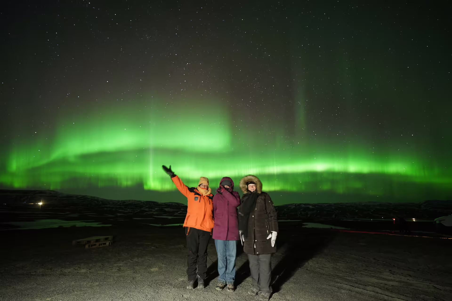 Three tourists posing under vivid green northern lights aurora borealis on Iceland jeep tour at night